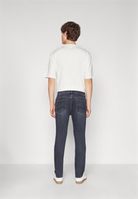 Camisa blanca de manga corta combinada con jeans ajustados azul oscuro que cuentan con bolsillos traseros y un diseño limpio y moderno. El calzado son zapatillas blancas.