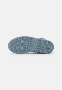 Modrý Nike tenisky podešev s kruhovými a mřížkovými vzory, logo značky uprostřed, vyfotografováno zespodu na bílém pozadí.