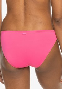 Roza bikini dno z brezšivnim dizajnom, izdelano iz gladkega materiala. Ima majhno oznako logotipa na hrbtni strani.