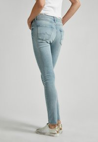 Vaqueros ajustados de color azul claro, confeccionados en denim, con bolsillos traseros de diseño minimalista en la costura. Combinados con una blusa blanca y zapatillas metálicas.