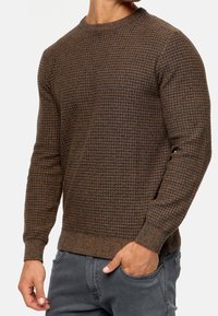 Brun tekstureret sweater med rund hals, der har et ternet mønster. Fremstillet af strikmateriale, tætsiddende stil og ribbede manchetter og kant.