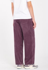Pantalones de pana en color malva con piernas anchas, con rayas horizontales y bolsillos en la parte posterior. Combinados con zapatillas grises que presentan detalles en azul.