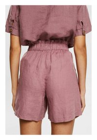 Shorts en lin rose clair avec une taille élastique, présentant une finition texturée et des revers roulés. Vue de dos montrant la chute du tissu.