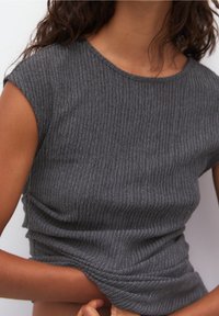 Top grigio a coste con maniche corte, caratterizzato da una scollatura rotonda e un tessuto strutturato. La maglietta appare aderente e leggermente arricciata in vita.