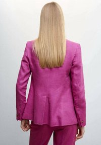 Blazer en lin fuchsia à coupe cintrée, avec fentes au dos et poignets boutonnés, assorti à un pantalon coordonné. Texture lisse, détails minimalistes.