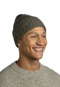 Gray knitted beanie with ribbed texture and a small brown logo patch, worn by a person in a light gray sweater with a crew neckline.