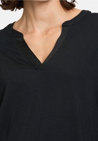 Svart V-ringad t-shirt gjord av mjukt tyg, med en glänsande svart trim runt halslinningen. Har en avslappnad passform för komfort.