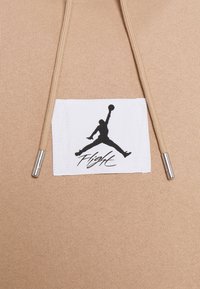 Felpa con cappuccio color beige con finitura strutturata, con una toppa bianca che mostra un logo Jordan nero e la scritta "Flight", e estremità dei lacci color argento.