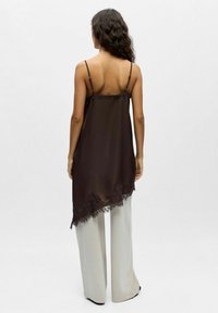 Camisole en satin marron avec bretelles ajustables, ornée d'une bordure en dentelle le long de l'ourlet et d'un design fluide, associée à un pantalon gris clair à jambes larges.