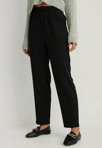 Czarne spodnie w paski z elastycznym pasem, o luźnym kroju i zwężanym nogawkach. W połączeniu z płaskimi czarnymi loafersami i jasnym swetrem.