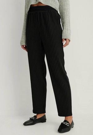 Sorte stribede bukser med elastisk livbånd, der har en løs pasform og tapered ben. Parret med flade sorte loafers og en lys farvet sweater.