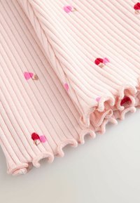 Tissu côtelé rose clair avec petits imprimés de champignons rouges et roses et bords froncés.