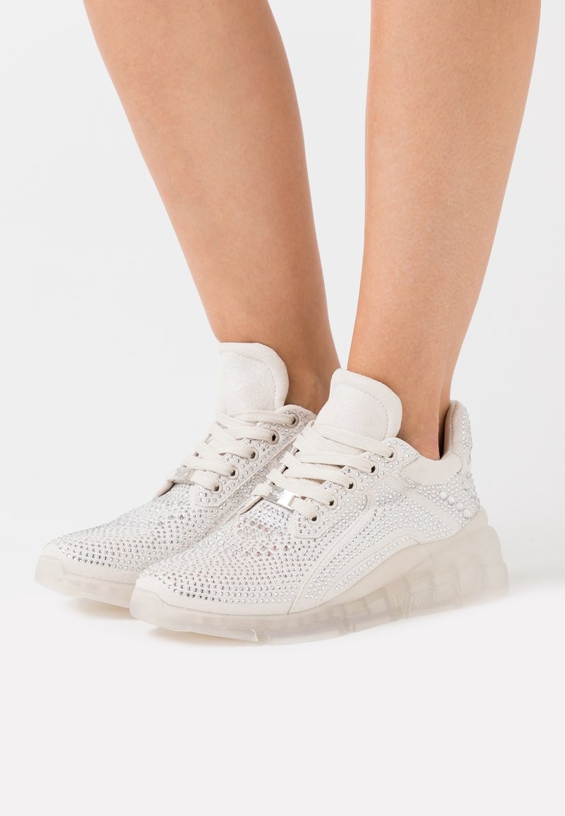 Baskets blanches avec un design en maille orné de strass, un col rembourré et une semelle en caoutchouc transparente.