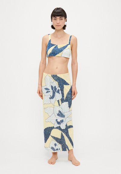 Twee-delig outfit met een gele crop top met blauwe accenten en een bijpassende lange rok versierd met bloemmotieven en pailletten.