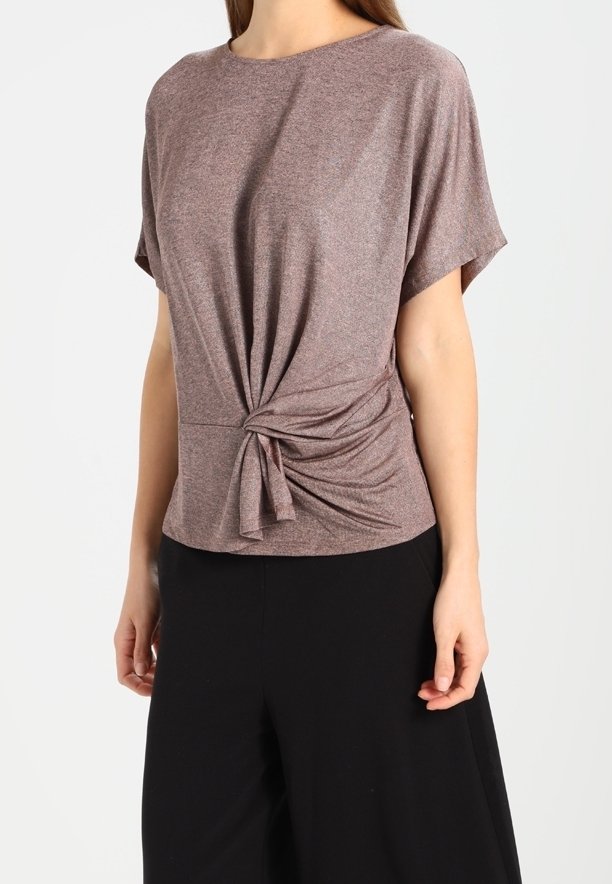 Haut marron à manches courtes en tissu doux et extensible avec un nœud décoratif à la taille et une coupe décontractée. Associé à un pantalon noir.