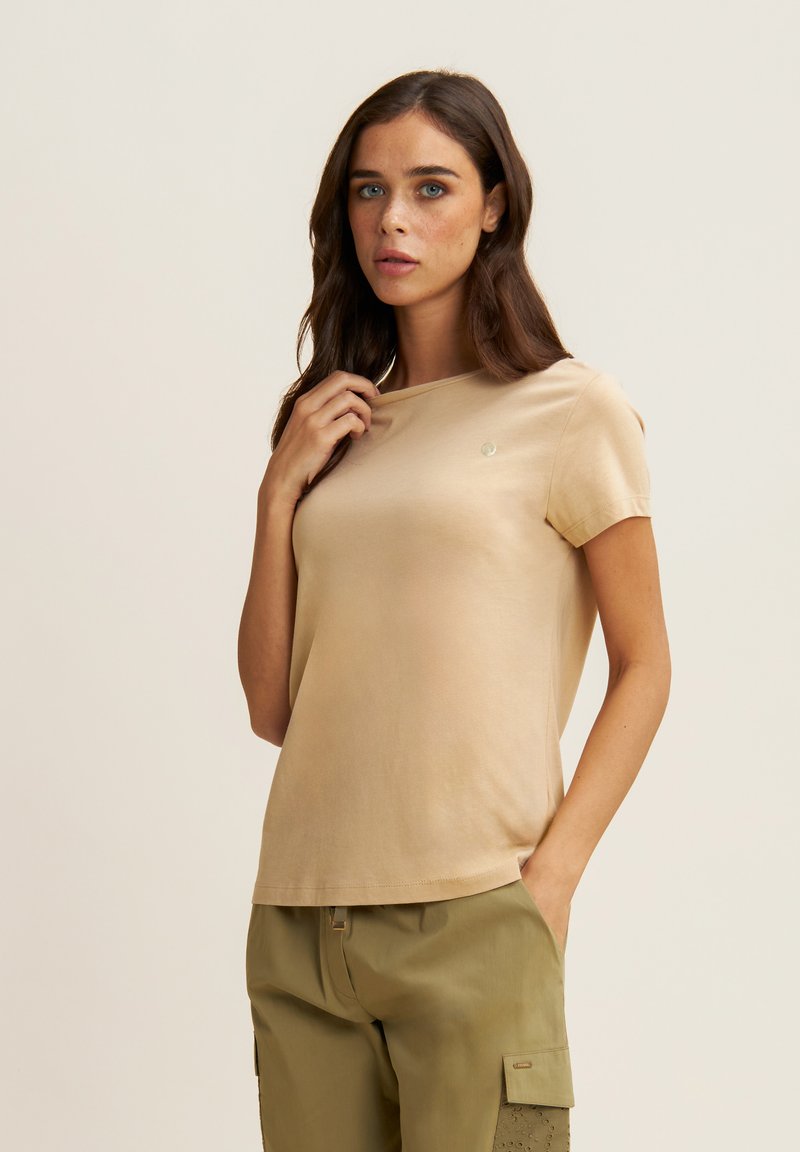 Camiseta de manga corta color beige hecha de tela suave; presenta un pequeño logo en el pecho y un corte relajado, combinada con pantalones cargo verde olivo.