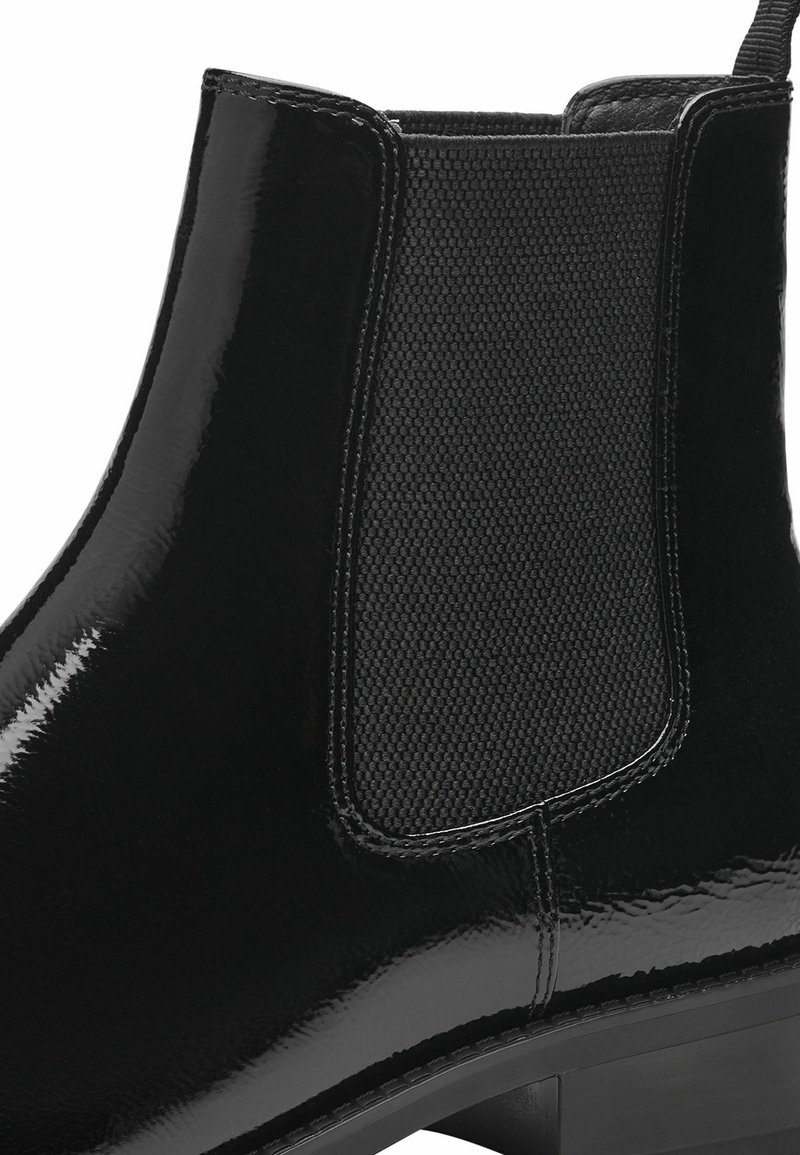 Bottine en cuir verni noir avec un panneau latéral élastique texturé, bout arrondi et petit talon empilé. Surface lisse avec finition brillante.