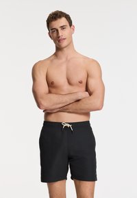 Schwarze Schwimmshorts mit elastischem Bund und beigem Kordelzug. Glattes Material mit geradem Schnitt und seitlichen Taschen.