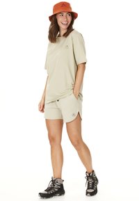 Ljusbeige oversized skjorta och matchande shorts. Orangea bucket hat med logotyp. Svarta och grå vandringsskor med snörning och vadderat ankelskydd.