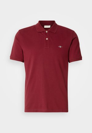 Burgundska polo majica od pamuka, s klasičnom ovratnikom, kratkim rukavima, dva dugmeta i malim logom na prsima.