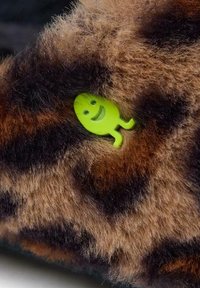 Fausse fourrure à motif léopard marron et noir avec une texture douce, présentant un accent de personnage souriant vert.