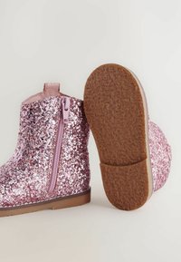 Glittriga rosa ankelboots med dragkedja på sidan, slät textur, brun gummisula och rund tån design.