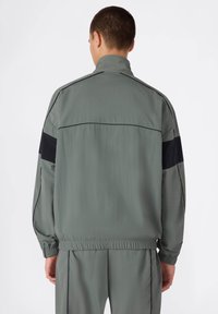 Szara, lekka kurtka z wysokim kołnierzem, elastycznymi mankietami i dołem, z czarnymi akcentami na ramionach, gładką teksturą i aerodynamicznym krojem.