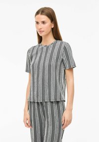 Short-sleeve top in black and white textured fabric with vertical stripes and a round neckline, featuring a cropped hem and loose fit.