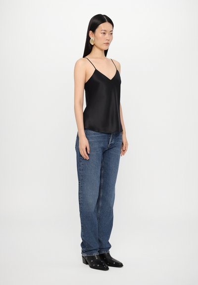 Camisole negru din satin cu bretele subțiri, purtat cu blugi drepti de culoare albastru deschis și cizme negre până la gleznă cu accente argintii.