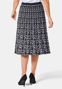 Jupe marine avec un motif géométrique blanc, à plis et à taille élastique. Portée avec des chaussures à talons hauts noires.