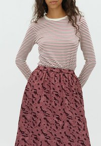 Haut à manches longues rayé en crème et bordeaux associé à une jupe maroon texturée présentant un motif de formes abstraites.