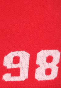 Piros kötött textil, amelynek felszínén nagy fehér számok, '9' és '8' láthatók puha, struktúrális mintázatban. Az anyag könnyű és rugalmas.