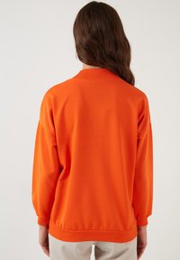 Bright orange sweatshirt with a relaxed fit, ribbed collar, and cuffed sleeves. Smooth texture, solid color, simple design.