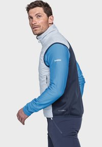 Leichter, hellblauer ärmelloser Weste mit hohem Kragen, Reißverschluss vorne, kontrastiert mit dunklen blauen Seiten, getragen über einem gerippten blauen Langarmshirt.