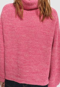 Roze gebreide trui met een hoge, geribbelde kraag. Heeft een ruime pasvorm en gekorrelde stof, met een kleine variatie in kleur doorheen.