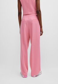 Pantaloni a gamba larga rosa realizzati in un tessuto morbido, con una texture liscia, due tasche posteriori e una vestibilità rilassata.