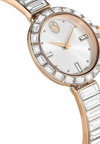 Montre en or rose avec un cadran argenté, des accents en cristal rectangulaires sur la lunette et le bracelet, et une forme fine et élégante. Fabriquée en Suisse.