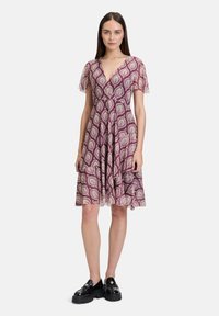 Bordeauxrotes Kleid mit floralen Mustern, kurzen Rüschenärmeln, tiefem V-Ausschnitt und ausgestelltem Saum; getragen mit schwarzen Plateauslippern.