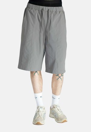 Light grey shorts with an elastic waistband and drawstring. Made of smooth fabric, knee-length with two front seams, paired with sneakers and socks.
