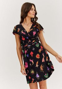 Čierne obväzové šaty s krátkymi rukávmi, ktoré majú farebné, eklektické vzory srdiec, očí, hviezd a zvierat. Dôraz na pás s mašľou.