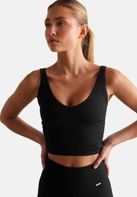 Zwarte geribbelde crop top met een diepe V-halsontwerp. Heeft dikke schouderbanden en een aangesloten silhouet, waarmee een gestructureerde stof wordt getoond.
