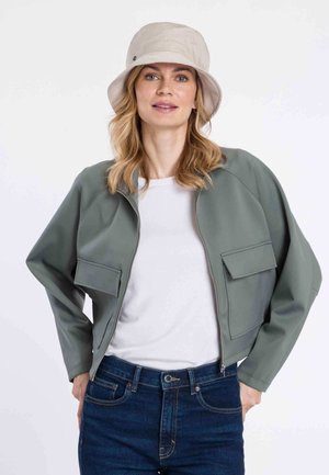 Hellgrüne Zip-Jacke mit zwei Vordertaschen, getragen über einem weißen Hemd und dunkelblauen Jeans. Verfügt über eine entspannte Passform und eine glatte Textur.