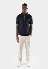 Mørk marineblå kortermet polo med glidelås krage, sammen med lyse beige bukser og hvite sneakers, på en nøytral bakgrunn.