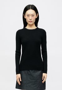 Μαύρο ριμπ πλεκτό πουλόβερ με μακριά μανίκια και στρογγυλή λαιμόκοψη, με ασημί διακοσμητικά χάντρες γύρω από το γιακά. Ομαλή υφή και εφαρμοστή γραμμή.