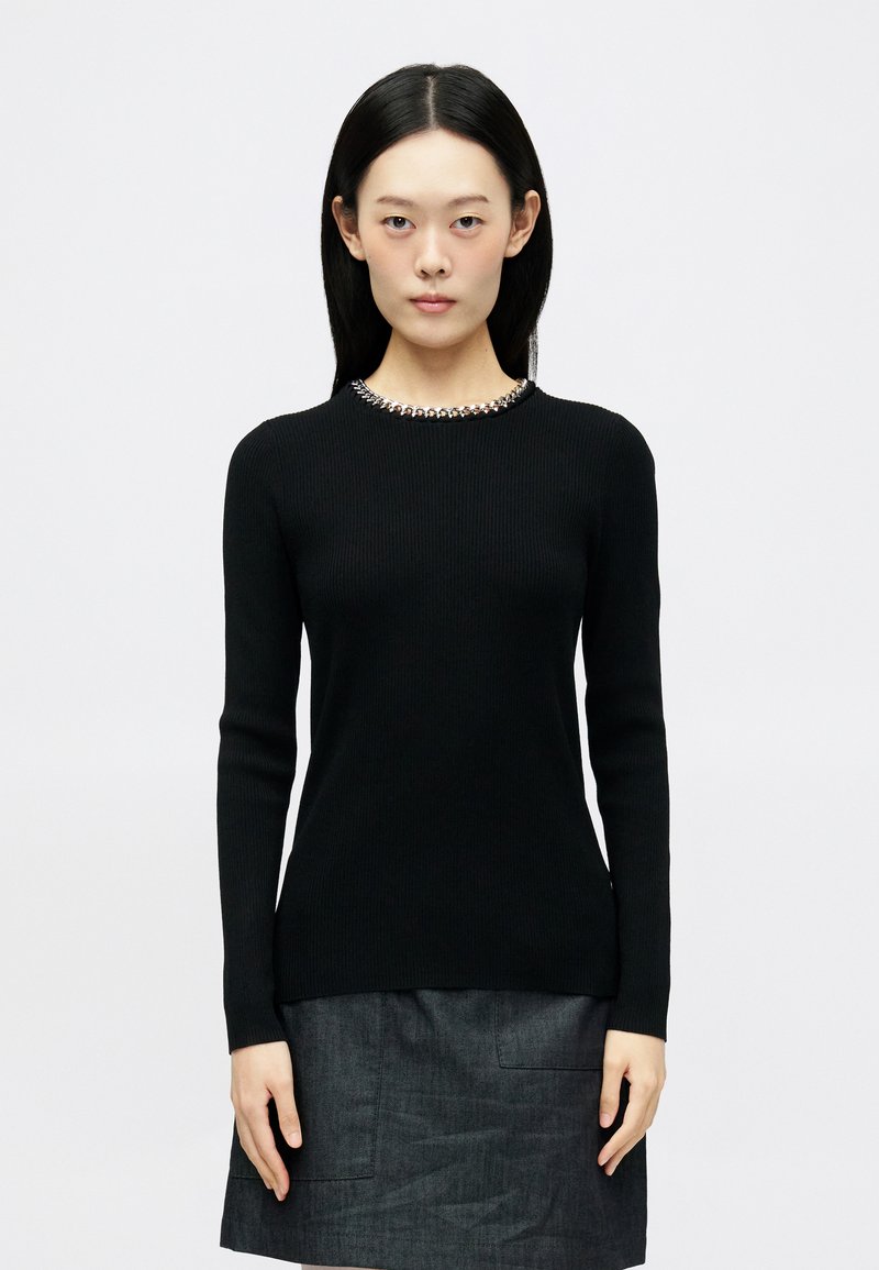 Μαύρο ριμπ πλεκτό πουλόβερ με μακριά μανίκια και στρογγυλή λαιμόκοψη, με ασημί διακοσμητικά χάντρες γύρω από το γιακά. Ομαλή υφή και εφαρμοστή γραμμή.