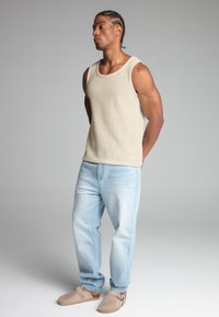 Top de tirantes de canalé beige, vaqueros de mezclilla azul claro y zuecos beige. El material parece suave con un corte relajado y un sutil detalle en el dobladillo.
