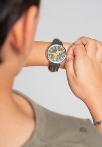 Montre-bracelet noire et orange avec un cadran rond, de grands chiffres jaunes et un design en silhouette de chien. Bracelet en caoutchouc avec des accents assortis.