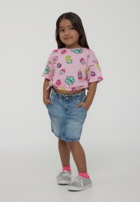 Camicia rosa a maniche corte con stampe colorate di gelati e fiori, abbinata a una gonna di jeans e sneakers argentee con calzini rosa.