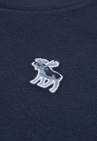Small embroidered moose in shades of blue on dark blue knitted fabric.