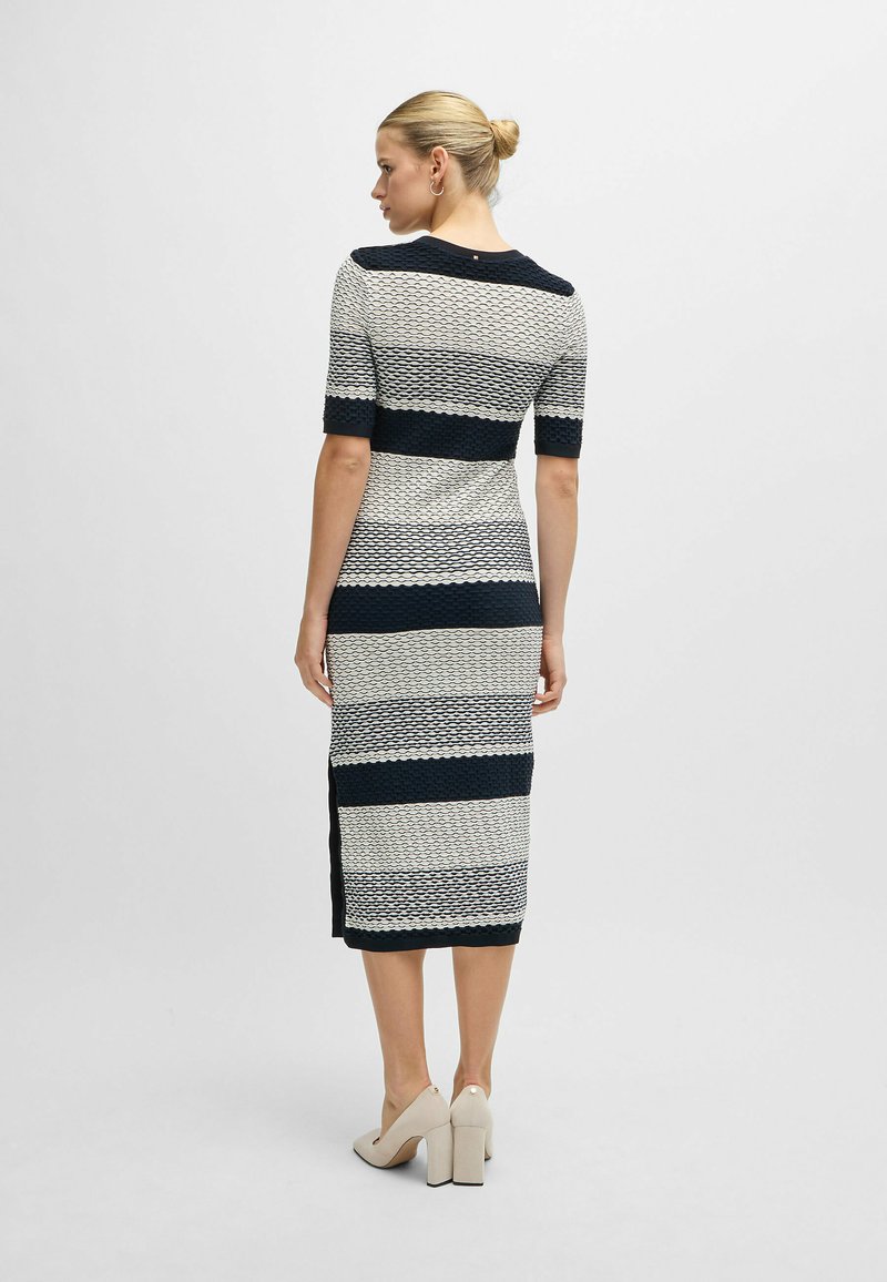 Strickkleid mit navyblauen und cremefarbenen horizontalen Streifen, kurzen Ärmeln und seitlichen Schlitzen. Kombiniert mit beigen Blockabsatzschuhen.